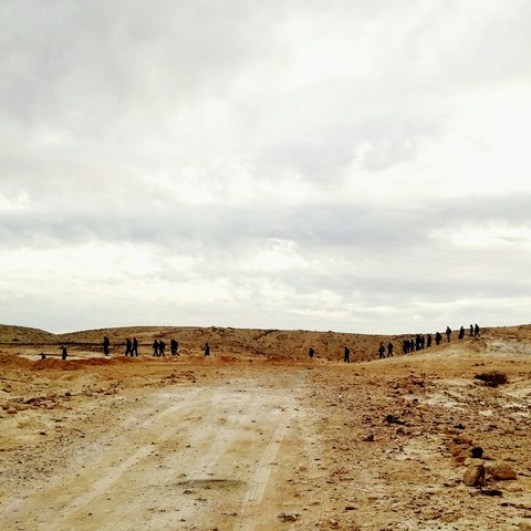 a convoy of people, walking towards the endless brown