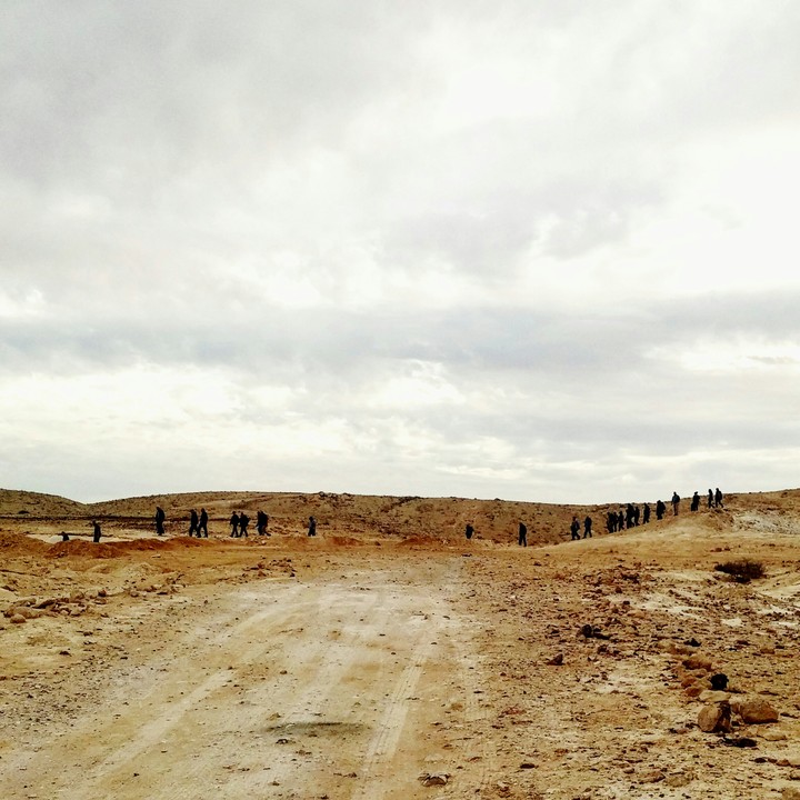 a convoy of people, walking towards the endless brown