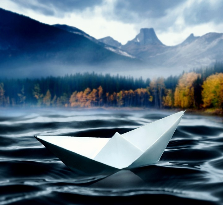 Paper boat in the lake against the backdrop of the mountains